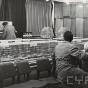 klatki z ptakami ustawione na stołach, kilka osób przygląda się ptakom