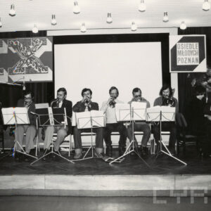 ośmiu mężczyzn siedzi na scenie i gra na instrumentach muzycznych