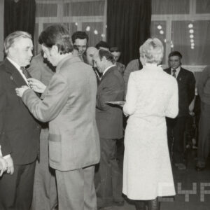 grupa ludzi stoi w pomieszczeniu, część z nich ma przypinane odznaczenia