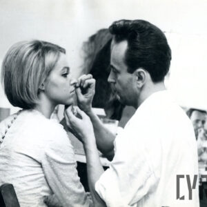 mężczyzna malujący młodą kobietę przed występem na estradzie, oboje ustawieni profilem