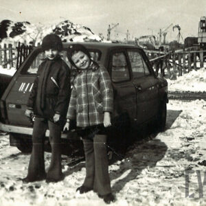 chłopiec i dziewczynka pozujący do zdjęcia na tle fiata 126p; w głębi drewniany płot i maszyny budowlane