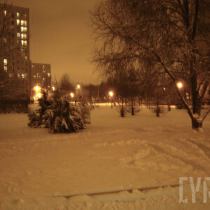 teren zielony z drzewami i placem zabaw zasypany śniegiem, otoczony blokami