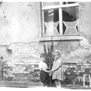 chłopiec z dziewczynką trzymają się za ręce, stoją na tle domu z cegieł