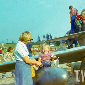 dzieci siedzące i stojące na skrzydłach samolotu ustawionego na trawie w parku