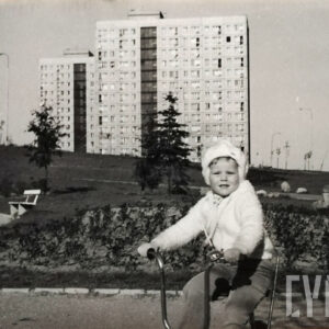 dziewczynka jadąca na trójkołowym rowerze; w tle bloki z wielkiej płyty