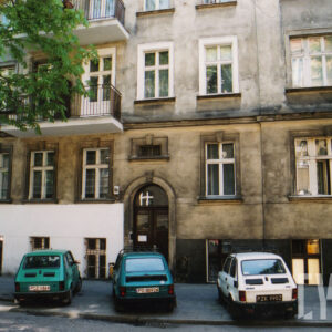 fragment fasady kamienicy z trzema dolnymi kondygnacjami, przed kamienicą zaparkowane samochody 