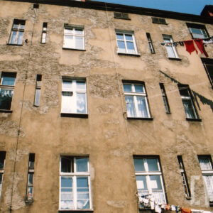 fragment ściany kamienicy z oknami, z prawej na rozciągniętych między oknami sznurach rozwieszone ubrania