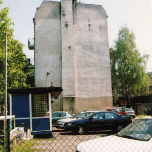 wysoka ściana budynku pozbawiona okien, na placu zaparkowane samochody