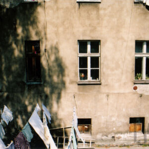 fragment ściany kamienicy z oknami, na rozciągniętych sznurach rozwieszone ubrania