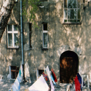 fragment ściany kamienicy z drzwiami i oknami, na pierwszym planie rozwieszone na sznurkach ubrania