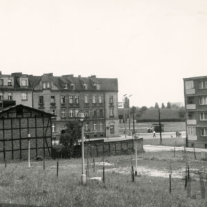 z lewej drewniano-ceglany dwukondygnacyjny budynek, w głębi kilkukondygnacyjne kamienice, z lewej fragment bloku mieszkalnego