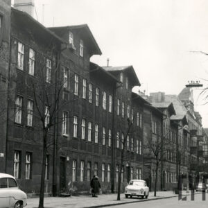 dwupiętrowe kamienice z mieszkalnym poddaszem, przed budynkami drzewa i zaparkowane na chodniku samochody