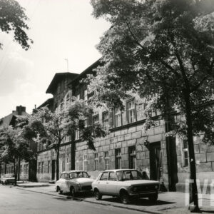 dwupiętrowe kamienice z mieszkalnym poddaszem, przed budynkami drzewa i zaparkowane na chodniku samochody