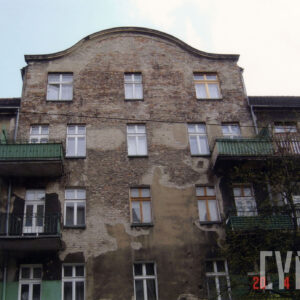 fragment elewacji kamienicy z balkonami i mieszkalnym poddaszem, w miejscu odpadniętego tynku widoczne cegły