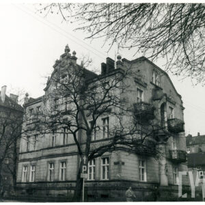 dwupiętrowa willa z suteryną, strychem i bogato zdobioną dekoracją rzeźbiarską, stoi w małym ogrodzie otoczonym metalowym płotem, przed nią drzewa