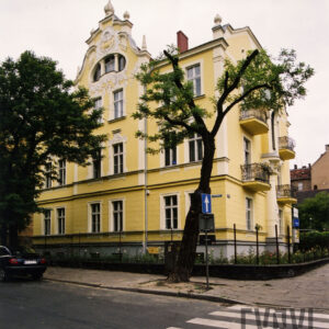 dwupiętrowa willa z suteryną, strychem i bogato zdobioną dekoracją rzeźbiarską, stoi w małym ogrodzie otoczonym metalowym płotem, przed nią drzewa