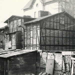 budynek mieszkalny drewniano-ceglany, przed nim niskie drewniane szopki