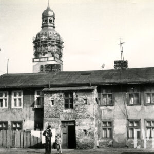 zaniedbany, dwukondygnacyjny budynek mieszkalny, na elewacji odpadający tynk, w głębi wieża kościoła, w górnej jej partii rusztowania