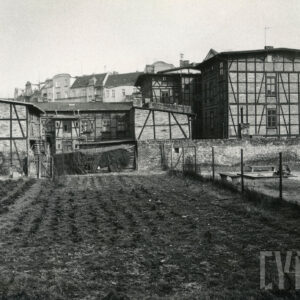 na pierwszym planie grządki, w głębi drewniano-ceglane domy mieszkalne