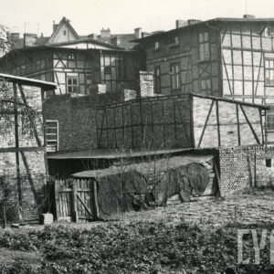 na pierwszym planie grządki, w głębi drewniano-ceglane domy mieszkalne