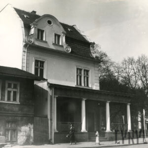 piętrowy budynek z mansardowym dachem z wejściem ozdobionym gankiem z kolumnami, które wspierają daszek, z lewej fragment przylegającego, niskiego budynku