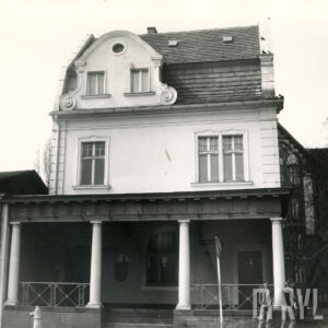 piętrowy budynek z mansardowym dachem z wejściem w formie ganku z kolumnami, które wspierają daszek