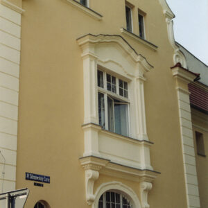 fragment ściany z oknami, dwa z nich zdobione dekoracją rzeźbiarską