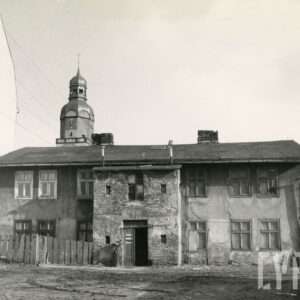 zaniedbany, dwukondygnacyjny prosty budynek, w głębi wieża kościoła