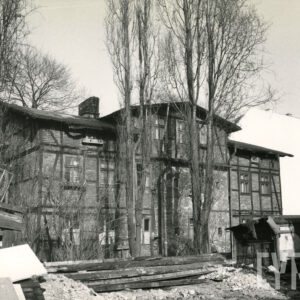 dwukondygnacyjny drewniano-ceglany budynek z mieszkalnym poddaszem, wokół niego drzewa