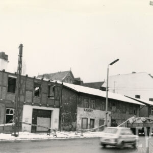 dwukondygnacyjne budynki, stojące wzdłuż ulicy, w trakcie rozbiórki, z prawej stoją dwie osoby, zimowa sceneria