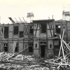 dwukondygnacyjny, drewniano-ceglany budynek w trakcie rozbiórki, przy nim leżące deski i cegły