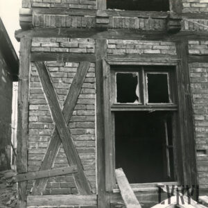 fragment elewacji budynku drewniano-ceglanego z otworem okiennym pozbawionym szyby i częściowo ram okiennych