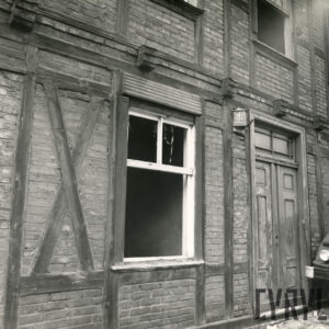 fragment ściany drewniano-ceglanego budynku z otworem okiennym pozbawionym szyb i częściowo ram okiennych oraz z drewnianymi drzwiami