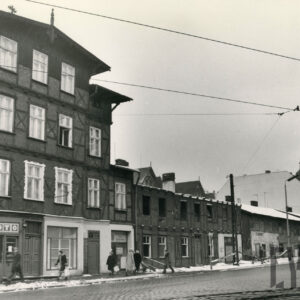 z lewej dwupiętrowy drewniano-ceglany dom narożny z mieszkalnym poddaszem, za nim trzy, jednopiętrowe budynki mieszkalne w trakcie rozbiórki