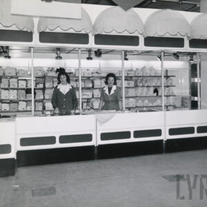 dwie kobiety w fartuchach przy ladzie, za nimi półki z artykułami