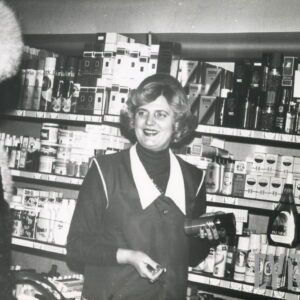 kobieta w fartuszku obsługuje klientkę (z lewej), za nią półki z artykułami kosmetycznymi