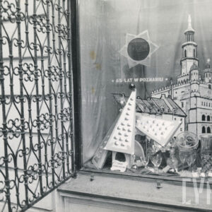 w oknie dekoracja złożona z rysunku ratusza i domków budniczych przed nimi ułożone kryształy, z lewej otwarta bogato zdobiona metalowa krata