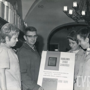 trzy kobiety i mężczyzna prezentują otrzymany dyplom, z lewej półki z artykułami na sprzedaż, u góry z prawej fragment metalowego żyrandolu