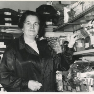 kobieta w ciemnym fartuchu na tle półek z ubraniami