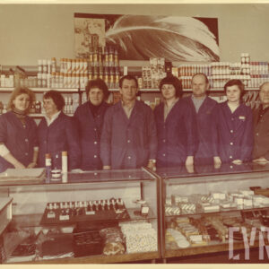 pięć kobiet i trzech mężczyzn w fartuchach pozuje do zdjęcia na tle półek z artykułami drogeryjnymi, przed nimi szklana lada