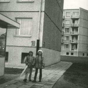 dwie dziewczynki ubrane w kurtki i berety na głowach stojące na tle bloków z wielkiej płyty