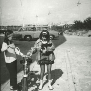 dziewczynki stojące przy rowerze na tle samochodów