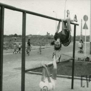 dzieci w czasie zabawy na trzepaku, w głębi bloki z wielkiej płyty