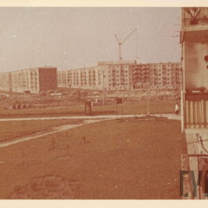 trawnik między blokami z wielkiej płyty, w oddali dźwig budowlany