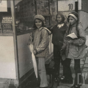 trzy dziewczynki przy kiosku, w głębi blok z wielkiej płyty