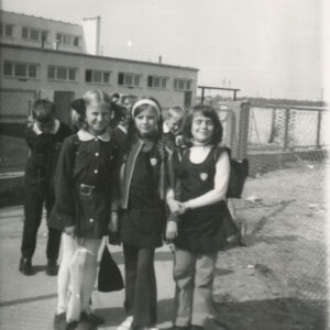 dziewczynki w mundurkach szkolnych z tornistrami na plecach, stojące na tle budynku z cegieł