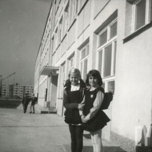 dziewczynki w mundurkach szkolnych z tornistrami na plecach, stojące na tle budynku z cegieł