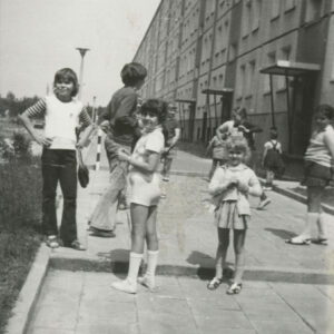 grupa dzieci bawiących się na chodniku przed blokiem z wielkiej płyty