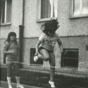 dziewczynki skaczące przez gumę na tle parteru bloku mieszkalnego