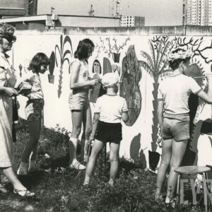 grupa dzieci z opiekunką malujących po płocie